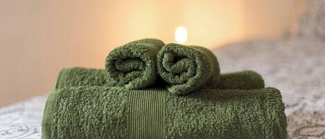A bed with rolled green towels and a lit candle in the background.