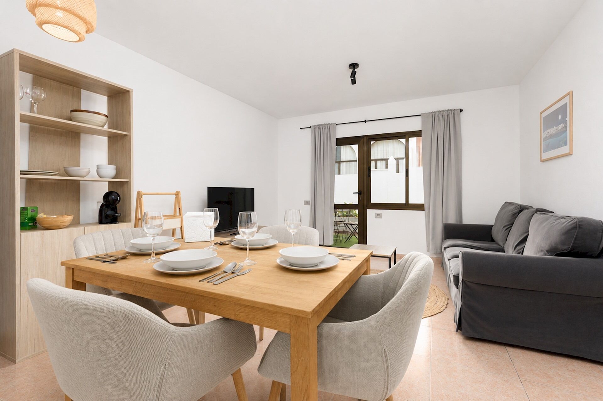 A dining area with a wooden table, white chairs, and a grey sofa.