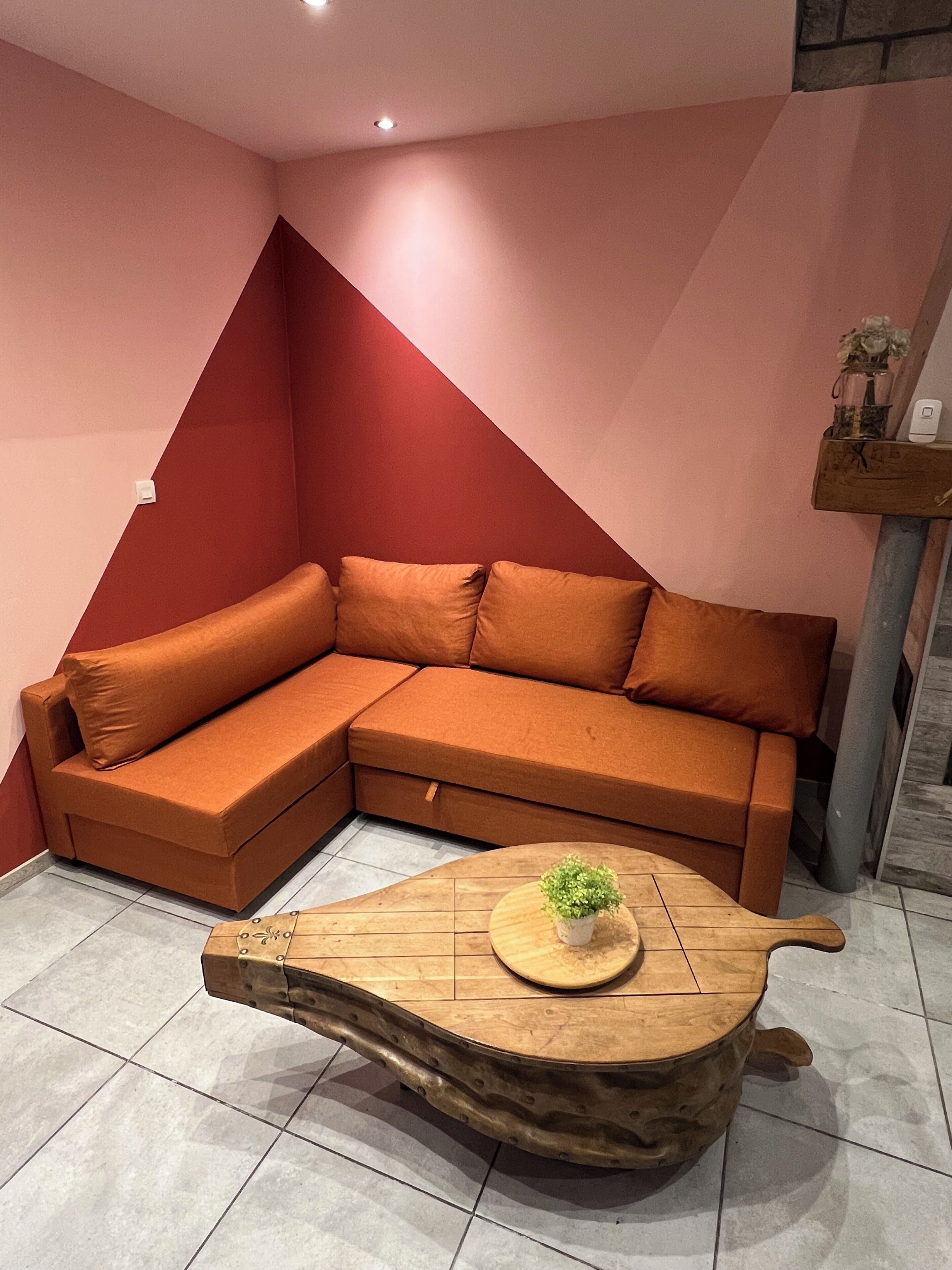 Sala de estar en esquina con sofá modular, una mesa de centro de madera con una planta y una pared de acento roja.