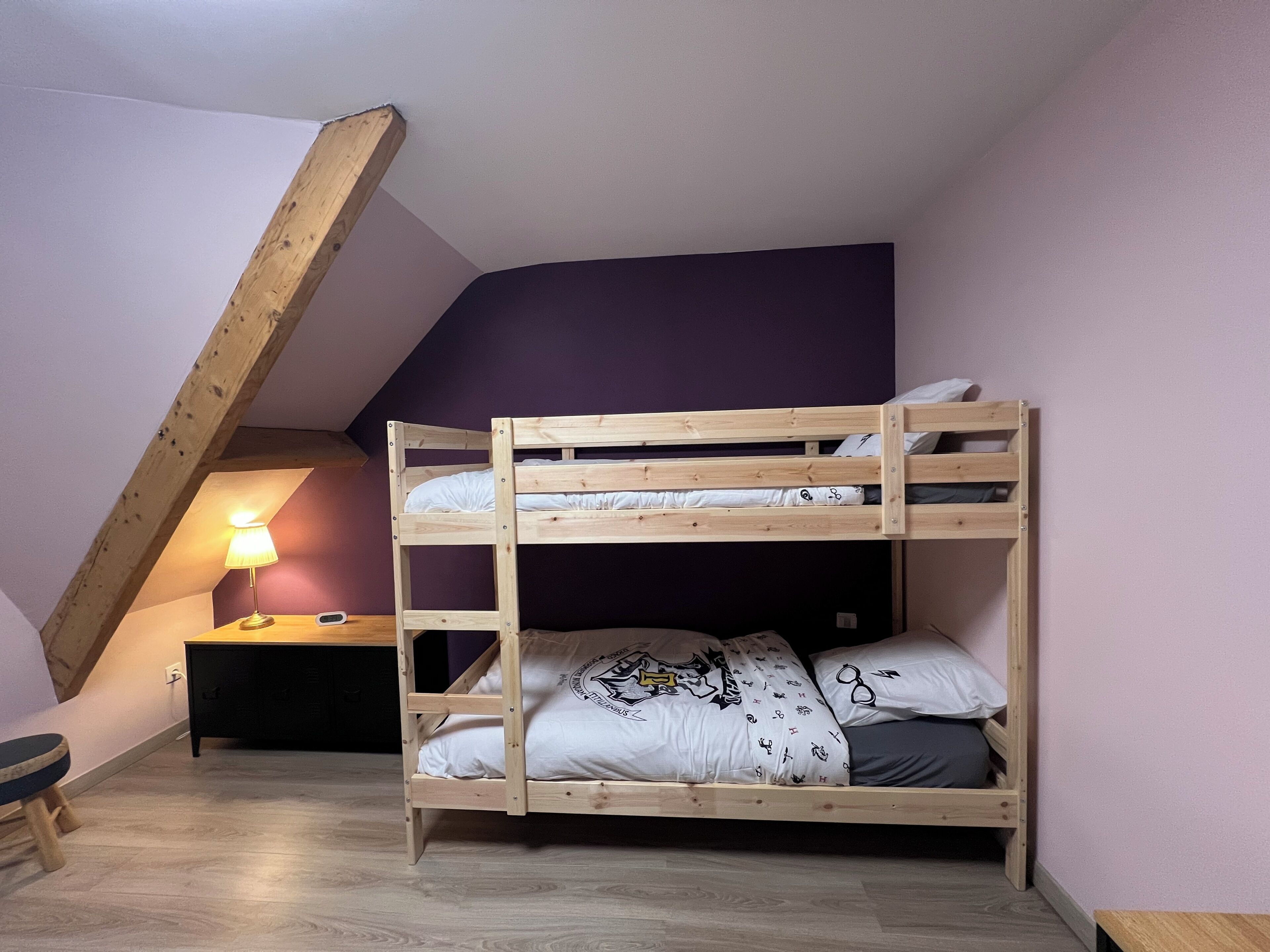 A bunk bed with a desk and lamp in a room with sloped ceilings.