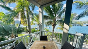 Una mesa de madera con dos sillas en un porche cubierto, con vista al mar y palmeras.