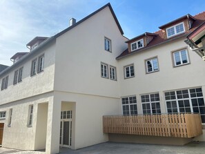 A multi-story building with a flat facade, large windows, and a wooden fence in front. - 119-square-meter newly built apartment with a garage in the heart of Germany's most beautiful historic city center (Bad Wimpfen)