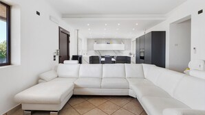 A modern living room with a white sectional sofa, a dining area with a table and chairs, and a kitchen area with cabinets and appliances. - 'Dimora Del Principe' with Sea View, Wi-Fi and Air Conditioning (Principe)
