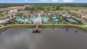 Ein Luftbild zeigt einen Ferienort mit mehreren Swimmingpools, darunter ein großer zentraler Pool, und einer Anlegestelle, die sich in einen See erstreckt.