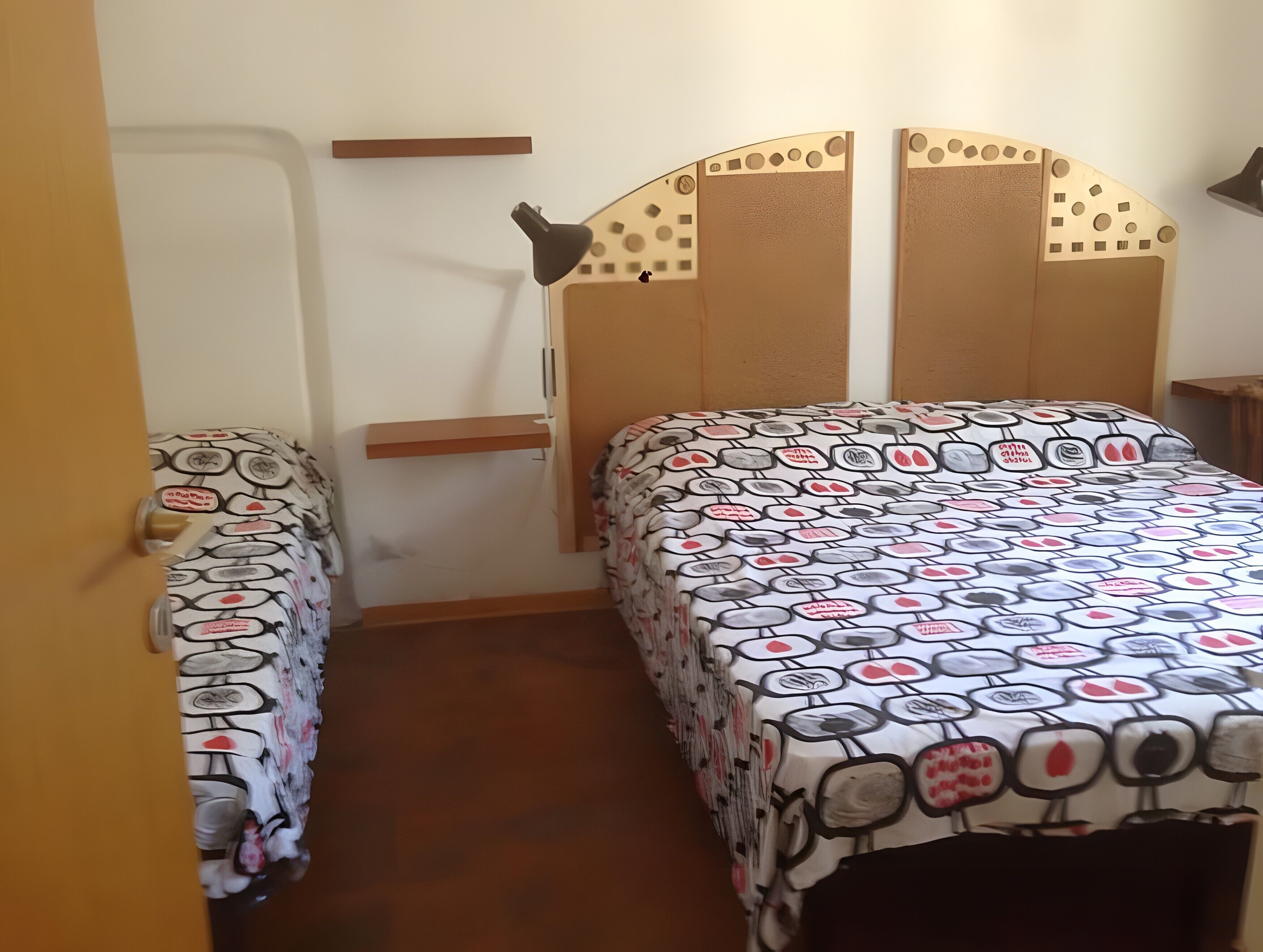 A bedroom with a bed, a nightstand, a wall-mounted shelf, and a door.
