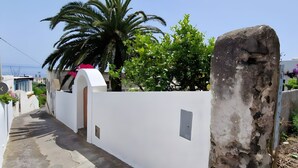 A narrow pathway leading to a white-walled building with a stone pillar, greenery, and a clear sky. - Casa Marel - Stromboli: Independent House with Garden and Two Terraces (Stromboli)