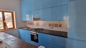 A kitchen with blue cabinets, a gas stove, a built-in oven, and a window with a view. - Casa Marel - Stromboli: Independent House with Garden and Two Terraces (Stromboli)