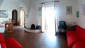 A living room with a red sofa, a television, and a dining area with a table and chairs. - Casa Marel - Stromboli: Independent House with Garden and Two Terraces (Stromboli)