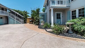 Ein zweistöckiges Gebäude mit überdachter Veranda, einer Treppe und einem Garten mit Vogelbad.