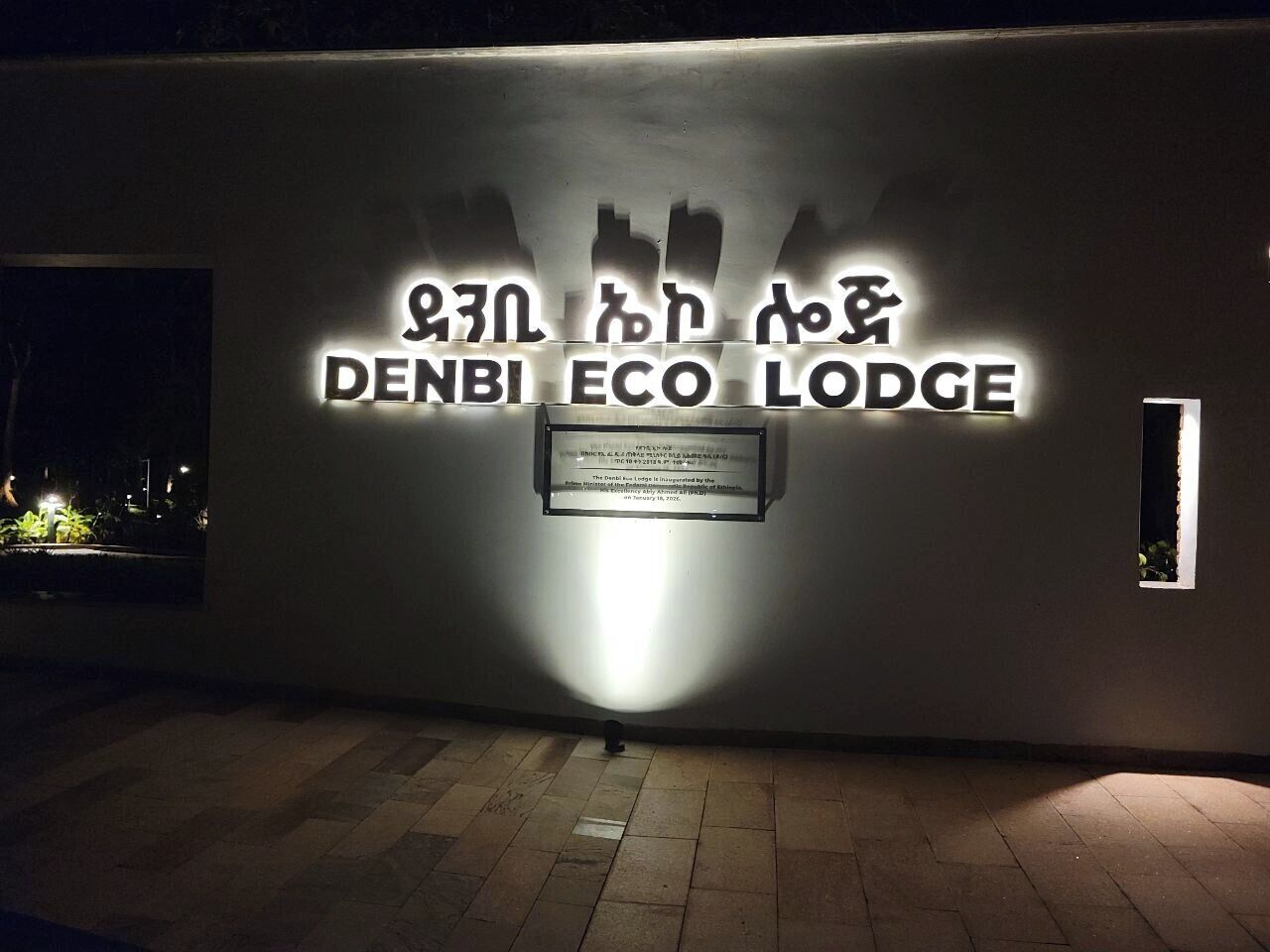 A wall with the text 'DENBI ECO LODGE' illuminated by a spotlight.
