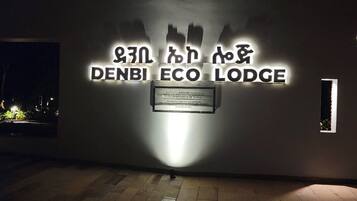 A wall with the text 'DENBI ECO LODGE' illuminated by a spotlight.