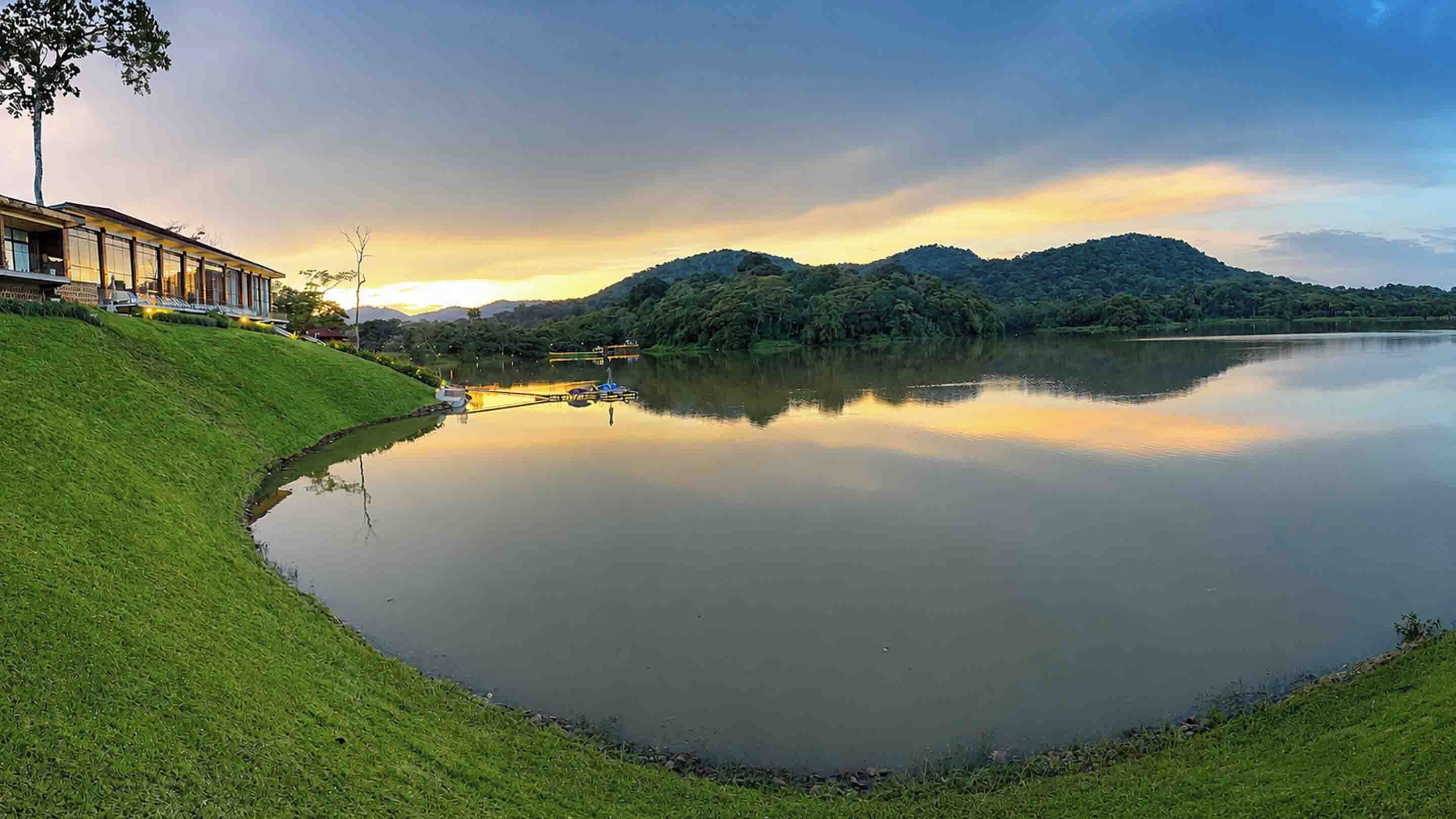 A calm lake with a grassy embankment and a building with large windows.