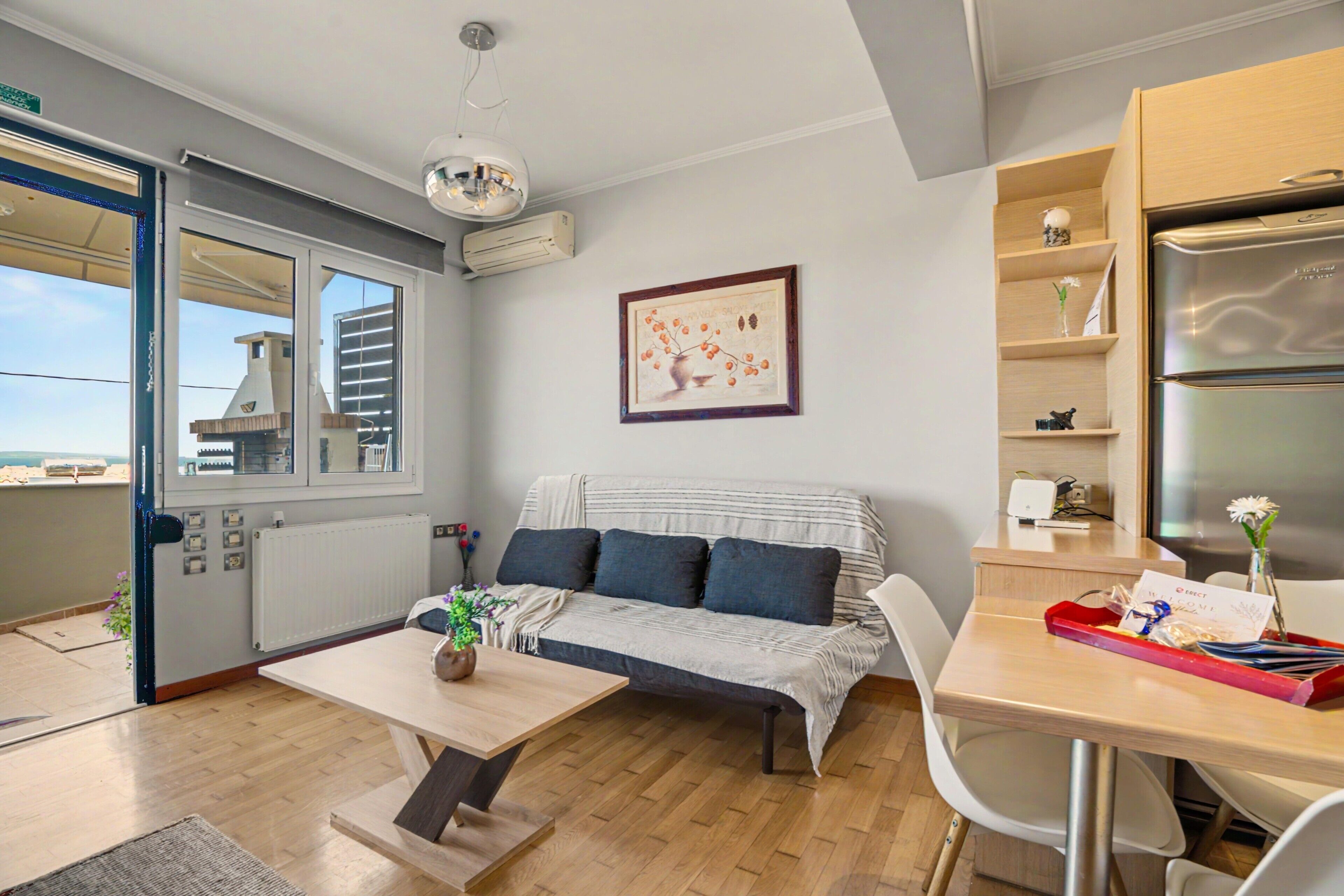 A modern living space with a sofa, a dining table, a kitchen area, and a window with a view.