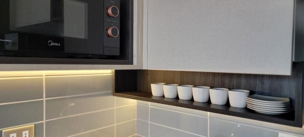 A kitchen with a microwave, a shelf with white cups, and a stack of plates.