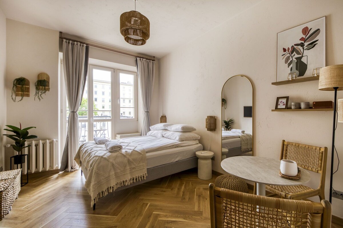 Een slaapkamer met een bed, nachtkastje, stoel, ronde tafel en een grote spiegel.