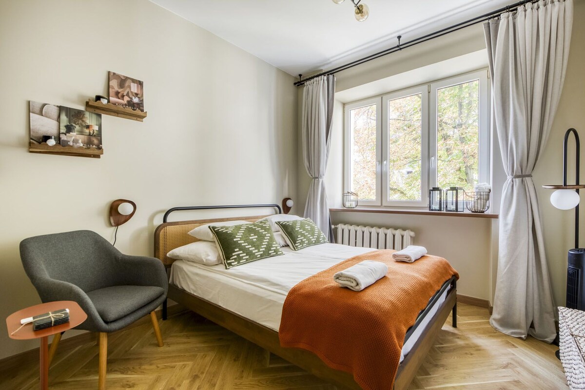 Een slaapkamer met een bed, een stoel, een radiator en een raam met gordijnen.