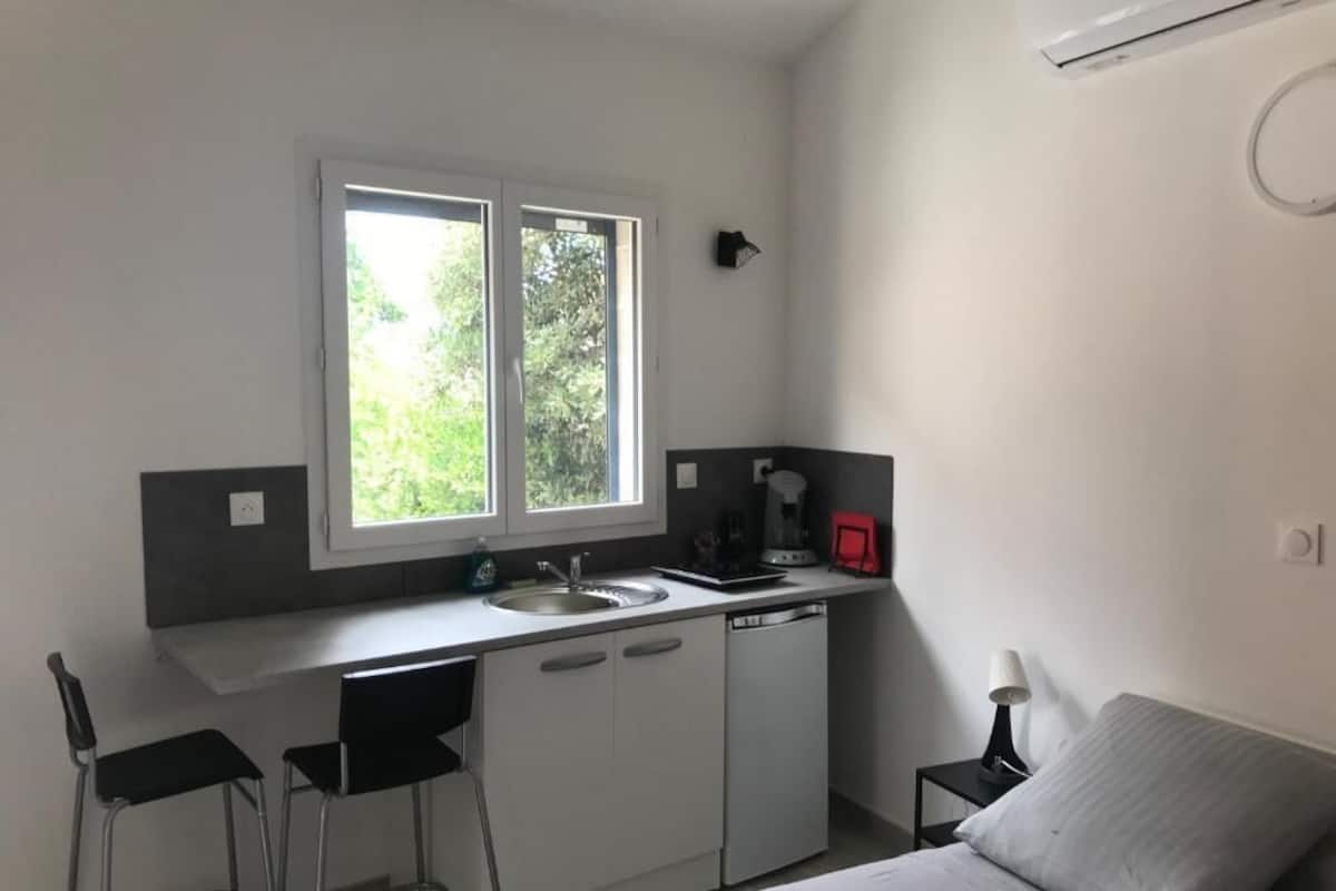 A compact room with a kitchenette, a bed, a window, and a small table.