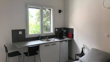 A compact room with a kitchenette, a bed, a window, and a small table.