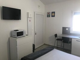 Una habitación con una cama, un escritorio con dos sillas, un televisor, un microondas y una puerta con un cartel.