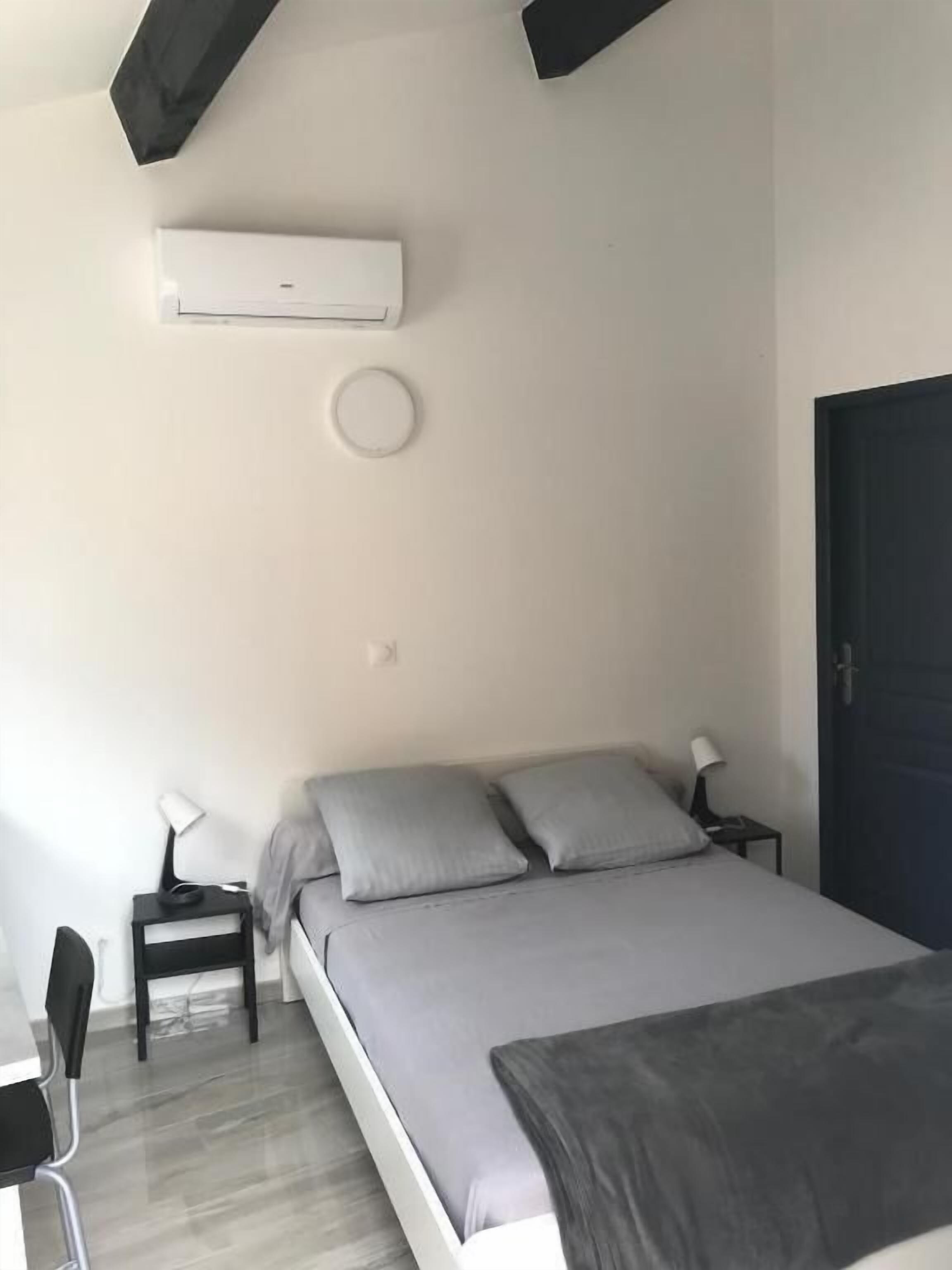 Une chambre à coucher comprenant un lit, des tables de chevet, un bureau, un climatiseur et une porte.