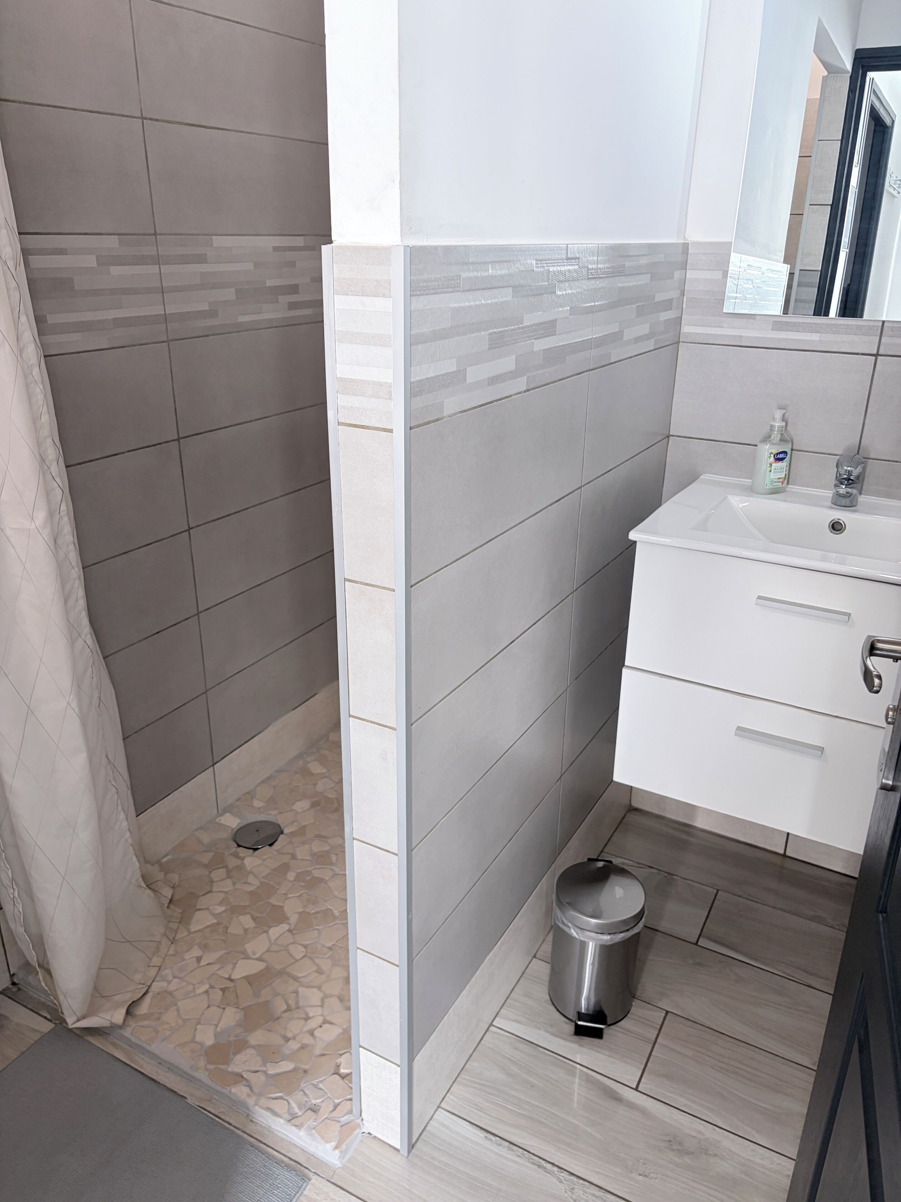 Un baño con ducha, lavamanos y cubo de basura.