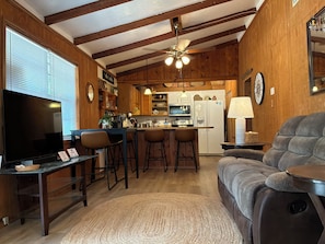 Eine gemütliche Küche mit Holzausbau, einer Bar, einem Esstisch mit Stühlen, einem Fernseher und einer Couch.