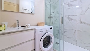 Une salle de bain moderne dotée d’une douche à parois de verre, d’un lave-linge encastré et d’un meuble-lavabo avec un miroir et un porte-serviettes.