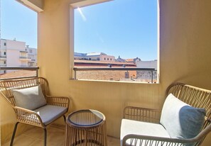 A balcony with wicker furniture, a small round table, and a view of buildings. - N&J - SABLE DORE - Balcony - Close sea (Nice)