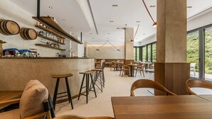 Un espace bar moderne avec des tabourets en bois, un comptoir où sont exposées des bouteilles et une vue sur la verdure à l’extérieur.