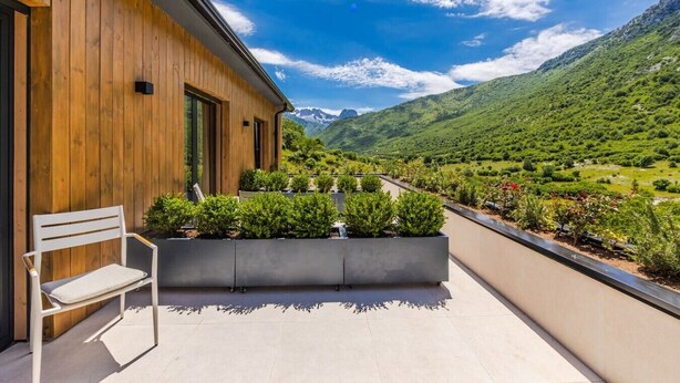 A balcony with a wooden wall, a white chair, and a view of a green valley and mountains. - Odat n`Bogë | Room 2 - Bjeshka | Breakfast Included by PikHost (Bogë)