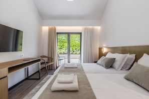 A modern hotel room with a flat-screen TV, a desk, two beds, a large window with curtains, and a view of greenery. - Odat n`Bogë | Room 2 - Bjeshka | Breakfast Included by PikHost (Bogë)