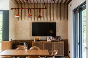 A modern kitchen with a large flat-screen TV, wooden cabinetry, and a dining area with a table and chairs.