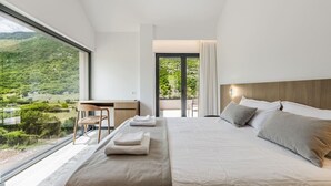 Een slaapkamer met een groot bed, een bureau en uitzicht op een groen landschap.