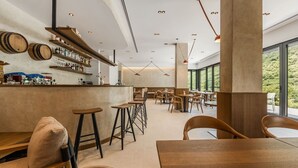 Een moderne bar met houten krukken, een toonbank vol flessen en uitzicht op groen door grote ramen.