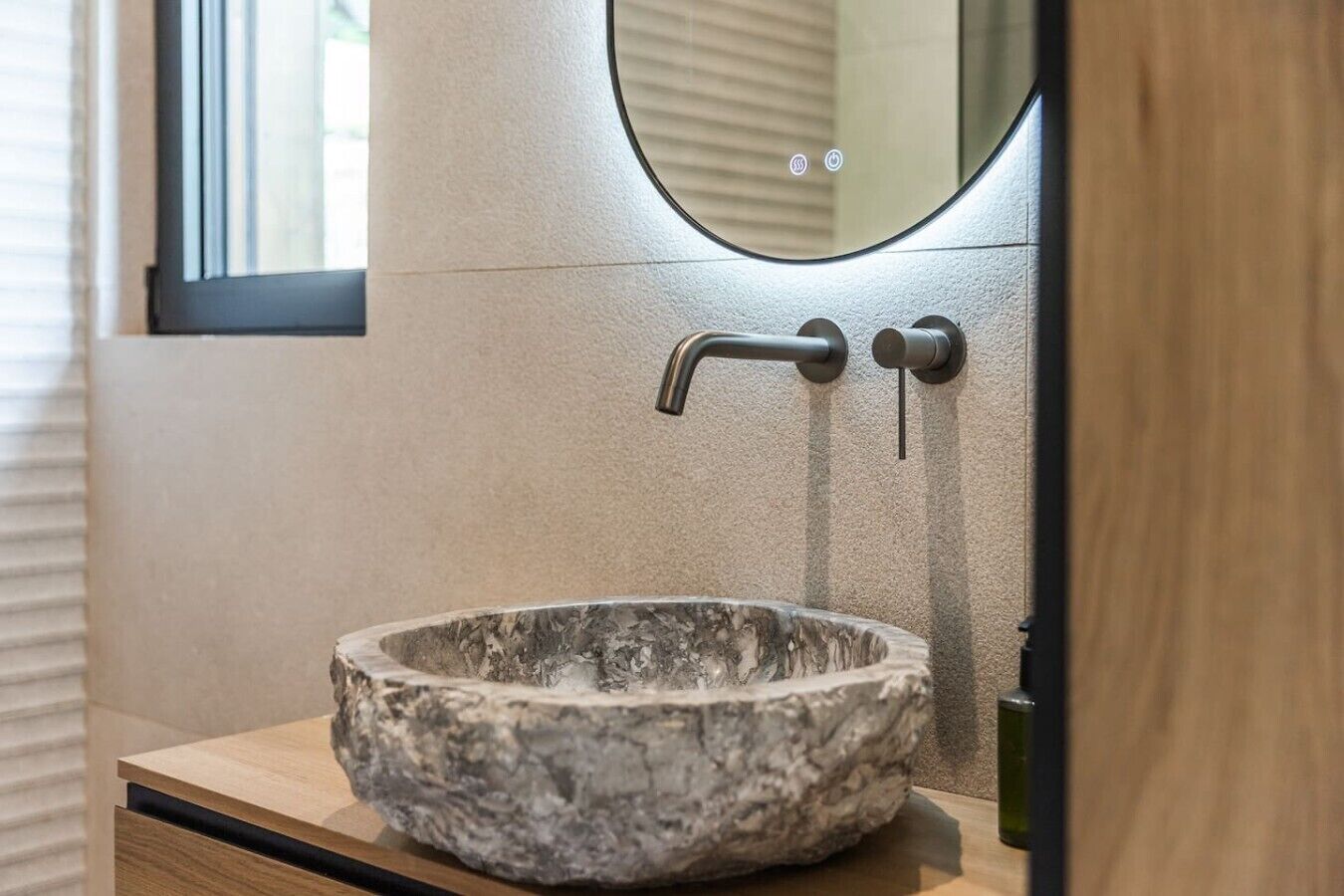 A stone sink with a modern faucet, a wooden countertop, and a mirror above.