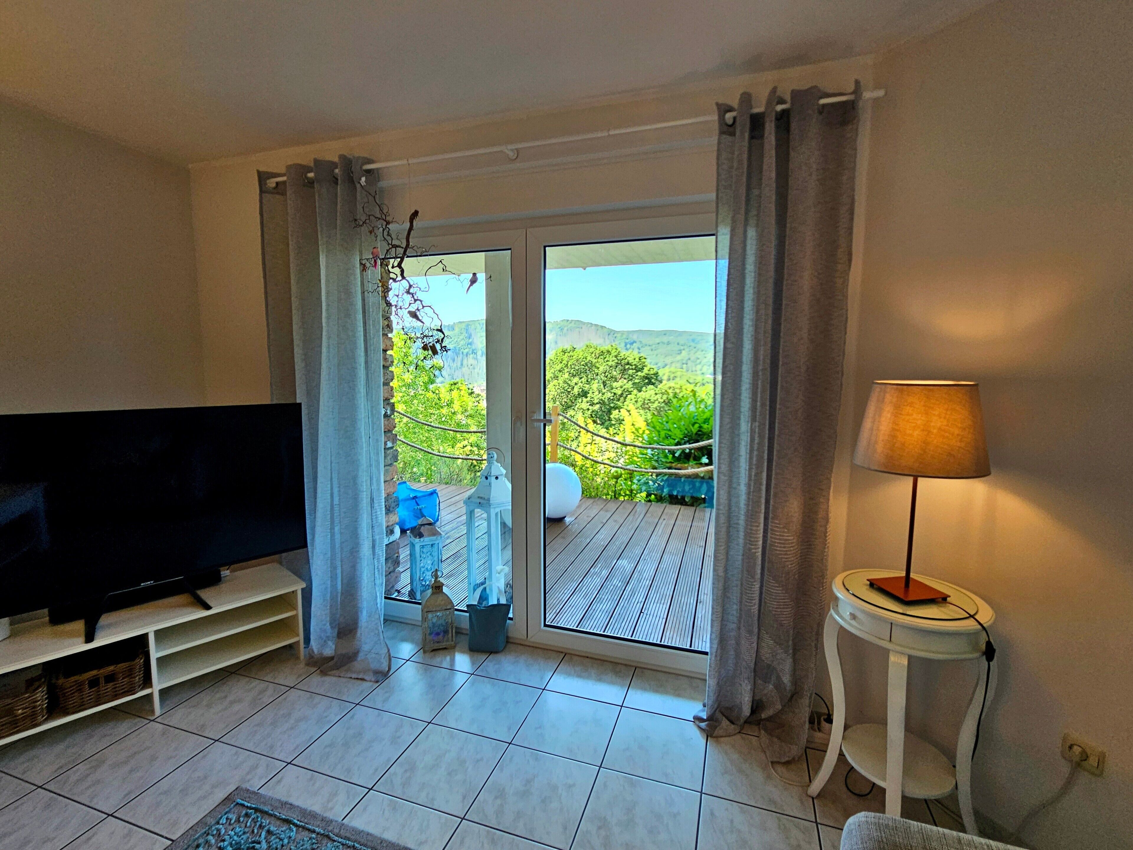 Un soggiorno con televisione, lampada e vista su un balcone con mobili da esterno.