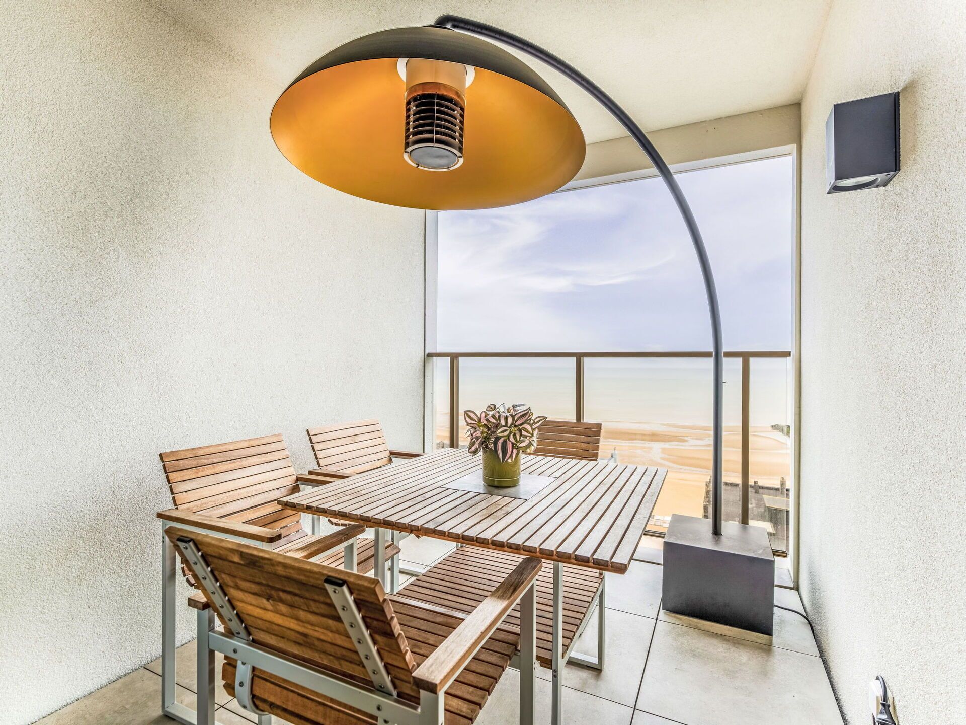 Un balcón con mesa y sillas, un colgante de luz y vistas a la playa.