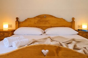 Una cama bien hecha con cabecera de madera, dos mesitas de noche con lámparas y un recorte con forma de corazón en la cabecera.