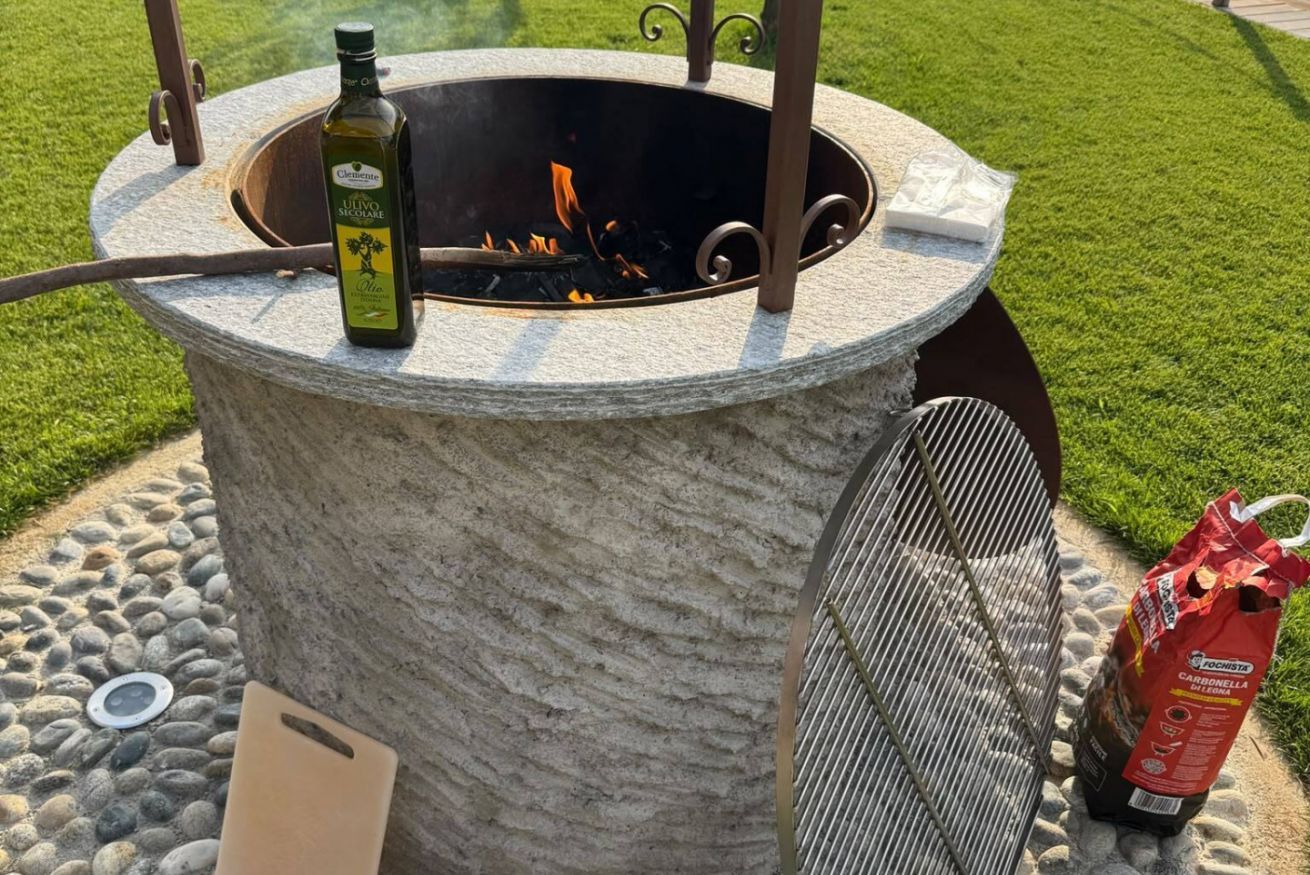 A stone fire pit with a bottle of olive oil and a bag of charcoal nearby.