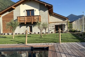 Una casa moderna con fachada de piedra, balcón de madera y una pequeña zona de piscina.