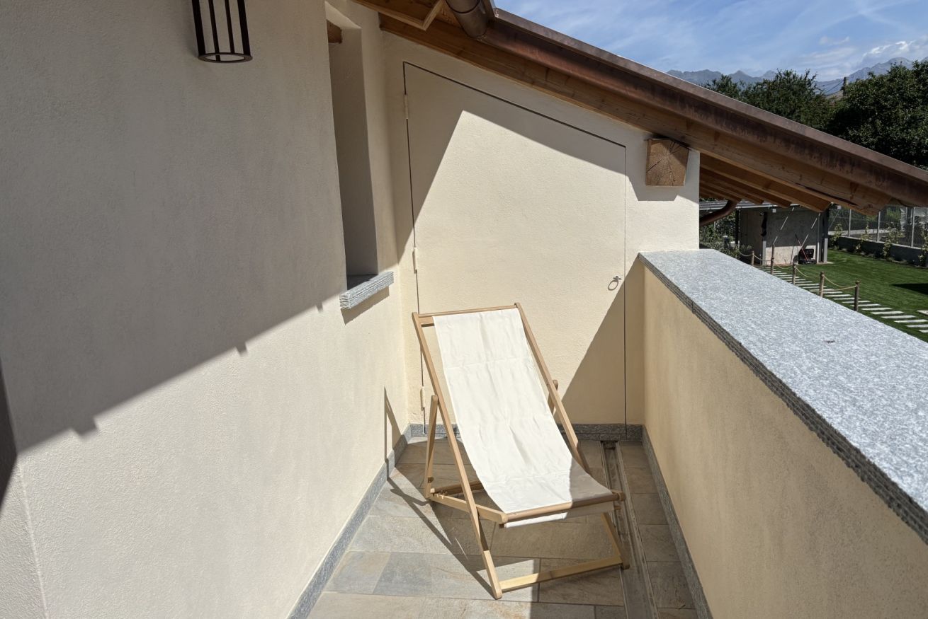 Un balcon avec une chaise en bois, un tissu blanc et une vue sur les montagnes.