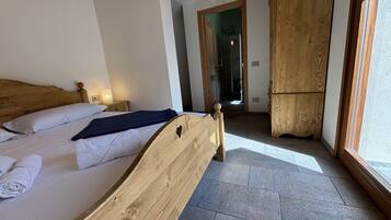 Ein Schlafzimmer mit einem Holzbett, einem Nachttisch, einer Nachttischlampe und Blick durch ein Fenster.