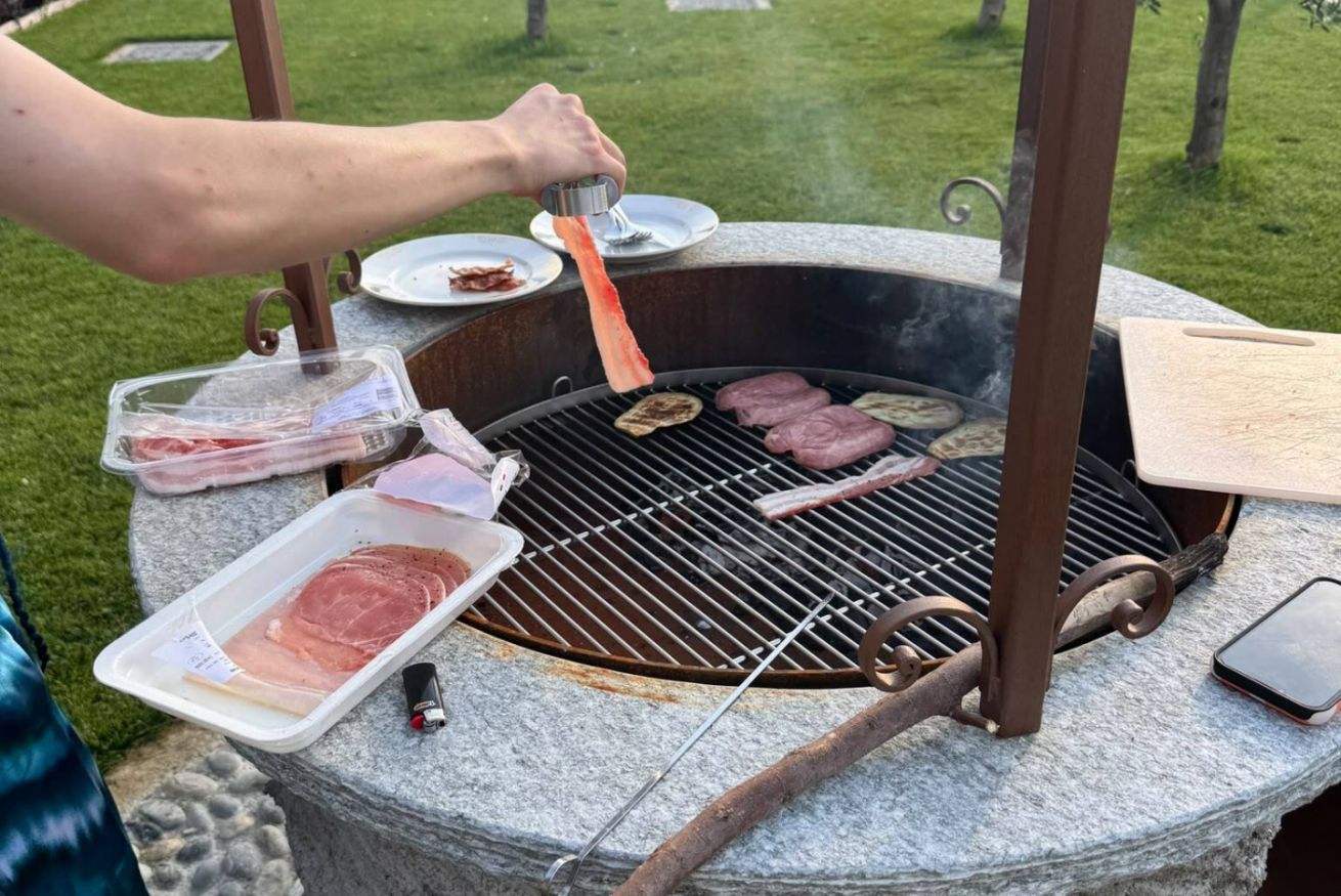 A person grilling meat outdoors with a portable grill on a stone surface.
