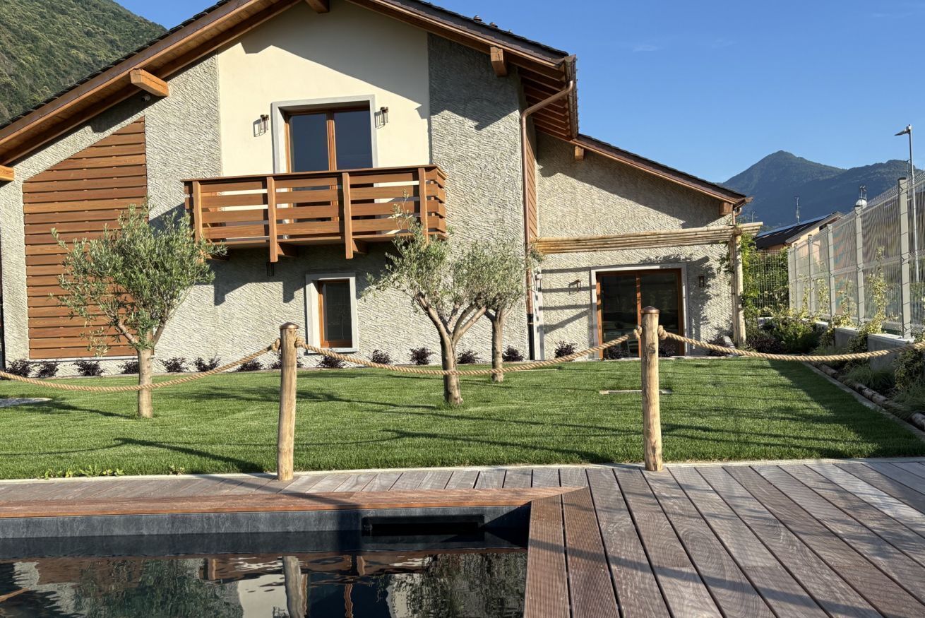 Ein modernes Haus mit Natursteinfassade, einem Holzbalkon und einem kleinen Poolbereich.