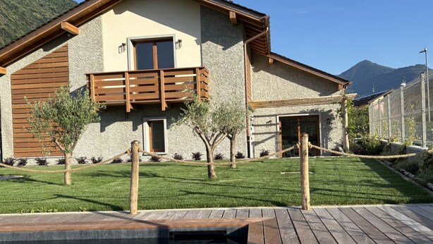 Una casa moderna con fachada de piedra, balcón de madera y una pequeña zona de piscina.
