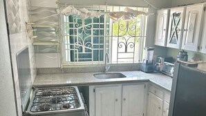 A kitchen with a gas stove, white cabinets, a sink, and a window with decorative bars.