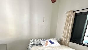 A bedroom with a bed, a window with curtains, a ceiling fan, and a tiled floor.