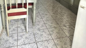 A room with a bed, a chair, a table, a window, and a refrigerator.