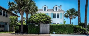 Ein zweistöckiges Haus mit geschlossenem Eingangstor, umgeben von Palmen und einer Hecke.