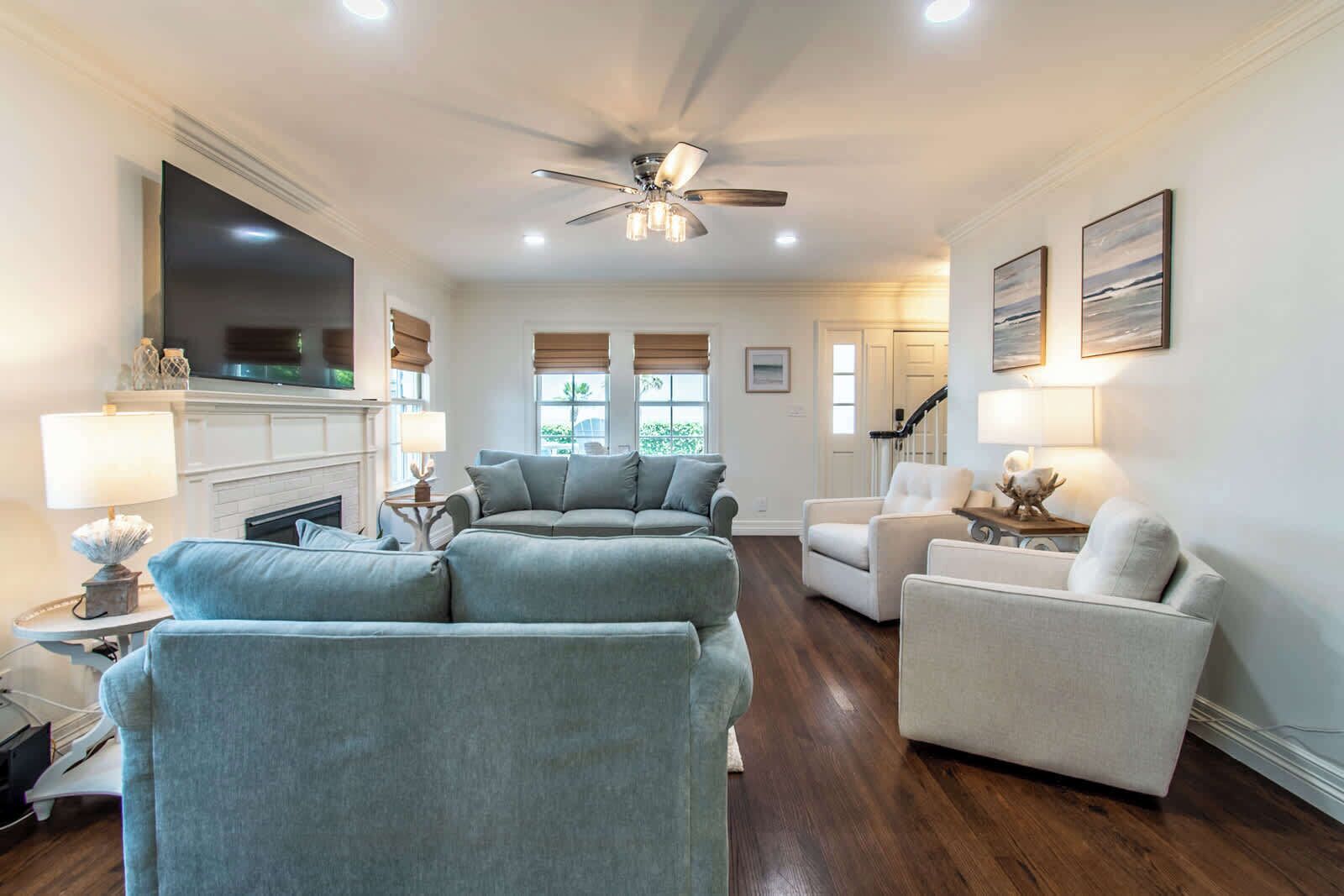 A living room with a fireplace, a ceiling fan, and a large TV.